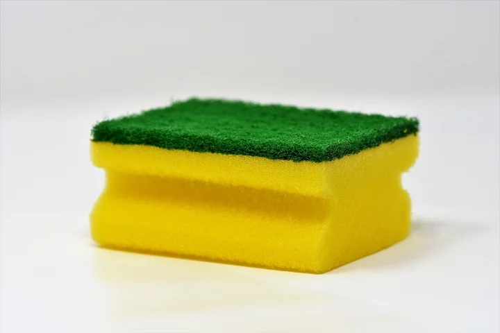 Yellow sponge with a green scrubbing pad on a white surface