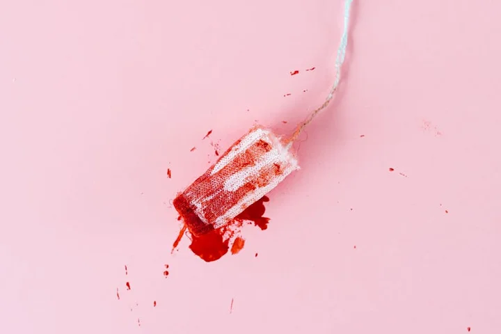 Blood-stained tampon on a pink background, illustrating a stain-removal decision scenario.
