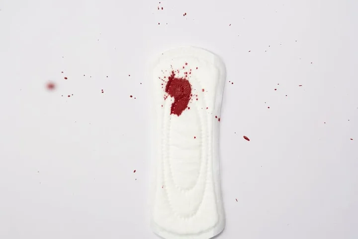 A white fabric wipe with a red stain on a white background, with small red specks nearby.