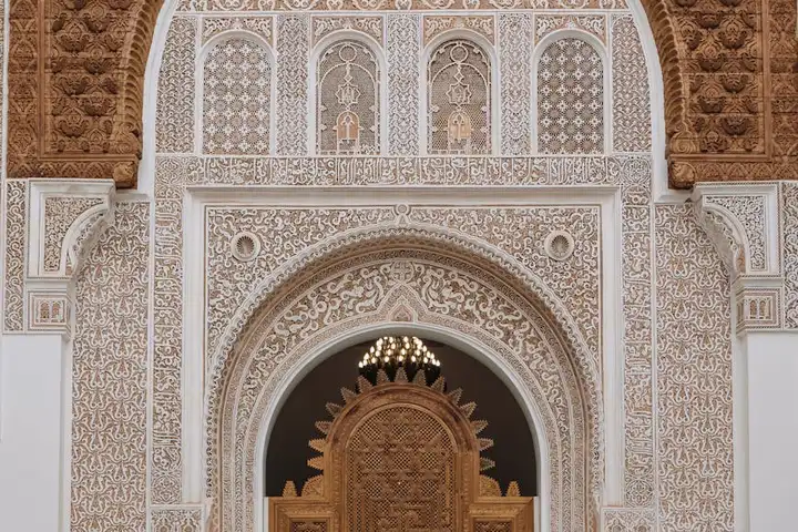Ornate white and beige tilework surrounding an arched doorway with intricate geometric patterns.