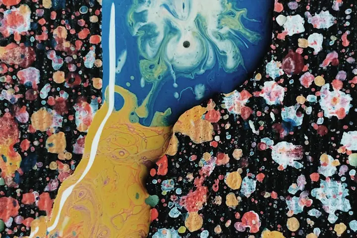Close-up of a yellow and blue swirled object on a colorful paint-splattered surface.