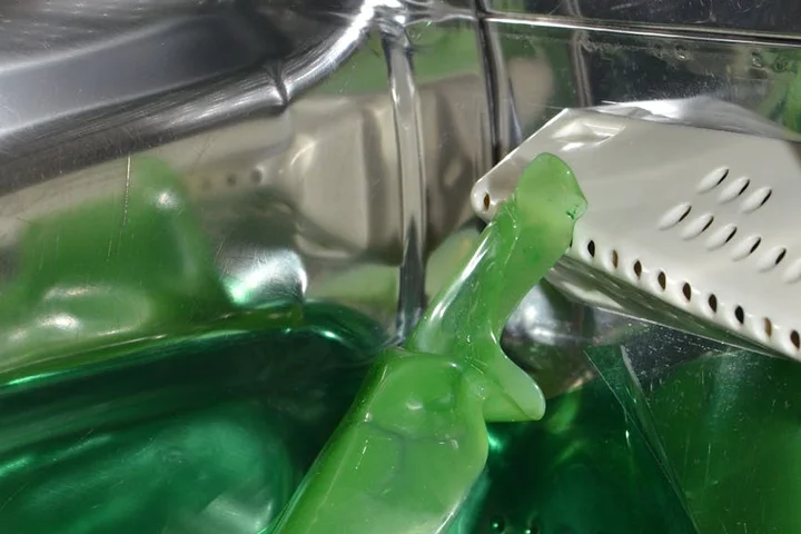 Green plastic toy inside a washing machine tub with green water, illustrating a stubborn stain context in laundry care.