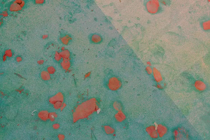 Close-up of a teal surface with orange-red spots scattered across, suggesting uneven or improper stain treatment.
