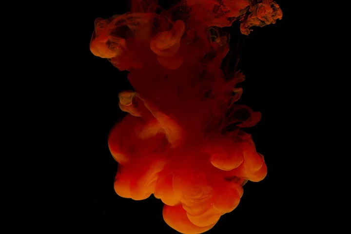 Red-orange dye diffusing in dark water against a black background, representing dye mobility during stain removal.