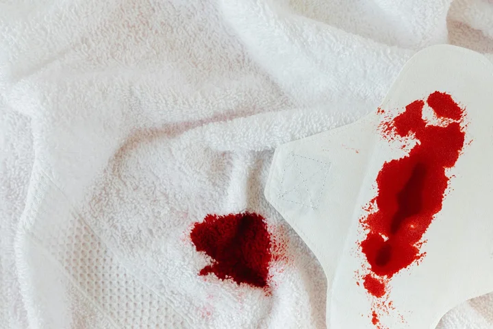 Close-up of white fabric with red stains and stained cleaning wipe, illustrating safety concerns when using stain-removal products.