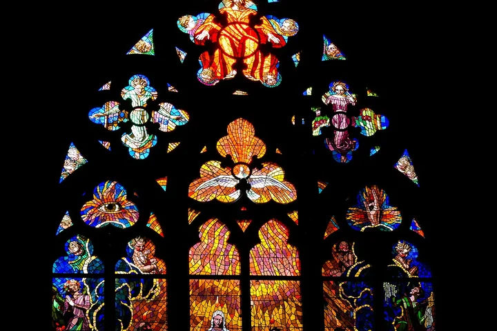 Colorful stained glass window with intricate patterns set against a dark background.
