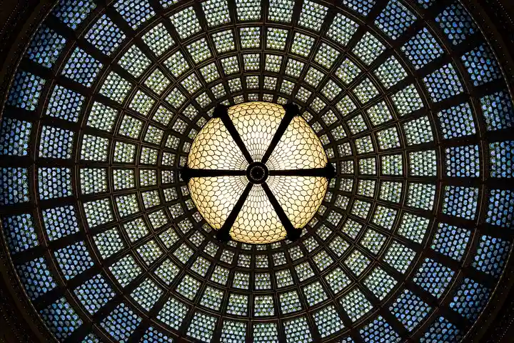 Close-up of a round stained-glass ceiling with a central hub and radiating patterns forming a circular mosaic.