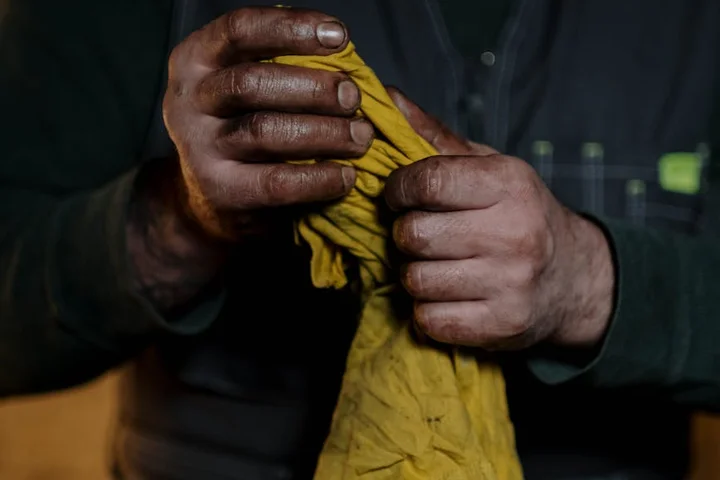 Close-up of a person's hands wringing a yellow cloth; the hands are stained with oil, illustrating hands-on stain removal.