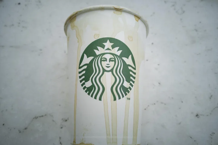 White paper Starbucks cup with brown coffee stains on a light marble surface.