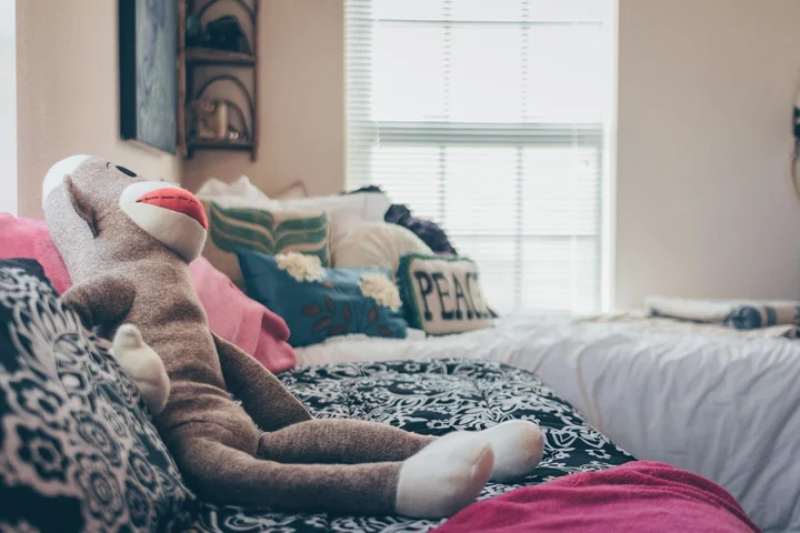 A cozy bed with layered sheets, cushions, and a plush stuffed monkey resting on the covers.