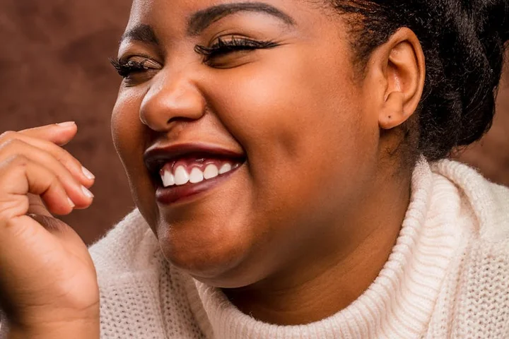 Close-up portrait of a smiling woman with dark skin wearing a cream knit sweater.