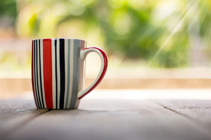 A striped ceramic mug on a wooden surface outdoors