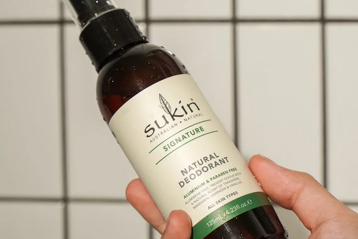 Hand holding a Sukin Natural Deodorant bottle against a tiled background
