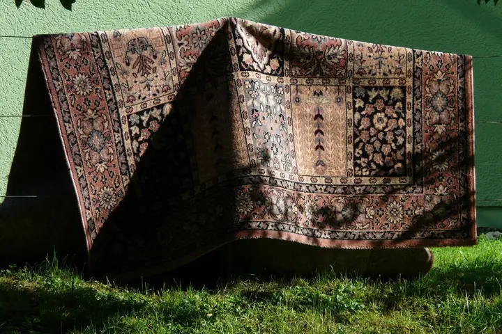 Patterned rug draped over outdoor furniture with a green wall and grass, illustrating a testing surface for carpet and car upholstery.