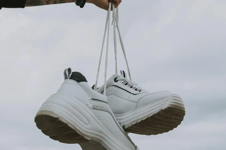 A pair of white sneakers suspended by their laces, showing different shoe uppers and materials.