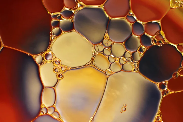 Macro photograph of interlocking oil droplets on a glossy surface with warm amber and gold tones.