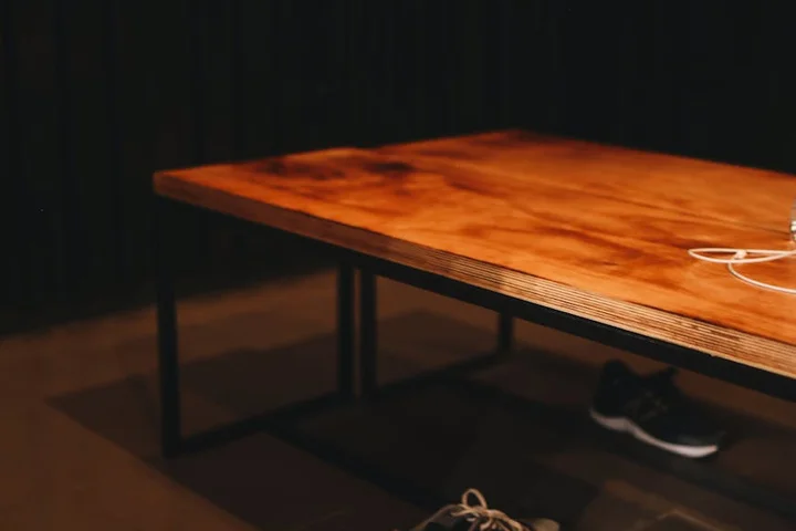 Dimly lit indoor scene showing a wooden table with shoes tucked underneath and tangled laces on the floor