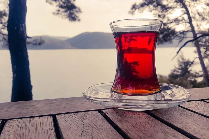 Glass of red tea on a wooden table outdoors by a lake with trees and hills in the background