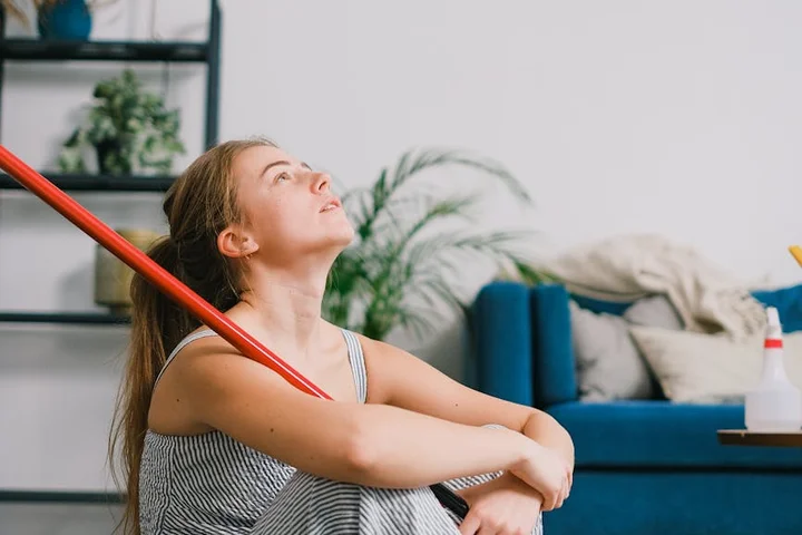 Woman sitting on the floor in a bright living room, resting with a red cleaning tool across her shoulders, illustrating terrazzo cleaning toolkit concepts.