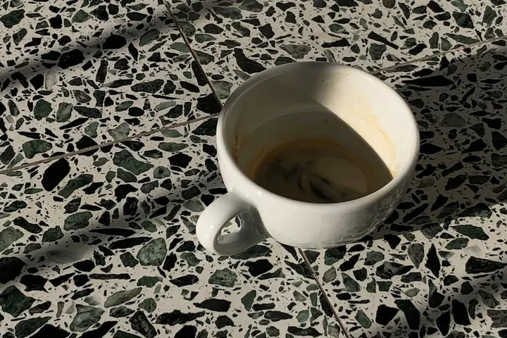 White coffee cup on a terrazzo floor with a coffee stain, illustrating common stains and the importance of sealers and smart cleaning habits.
