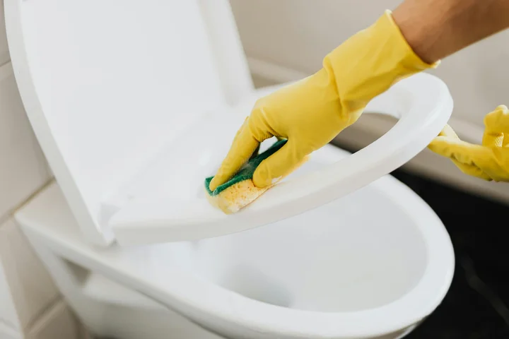 A person wearing yellow gloves scrubs the interior of a toilet with a sponge to remove rust stains.