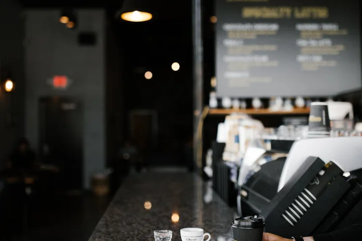 Close-up of a dark, polished granite countertop at a cafe, with blurred espresso machines and menu boards in the background.