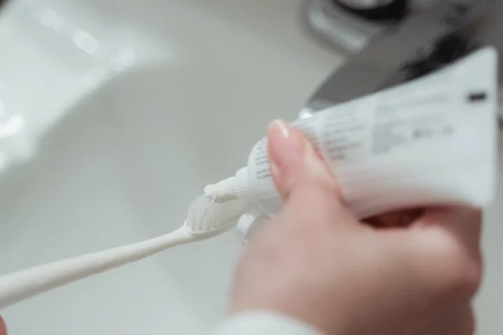 Close-up of a hand squeezing toothpaste onto a toothbrush over a bathroom sink.