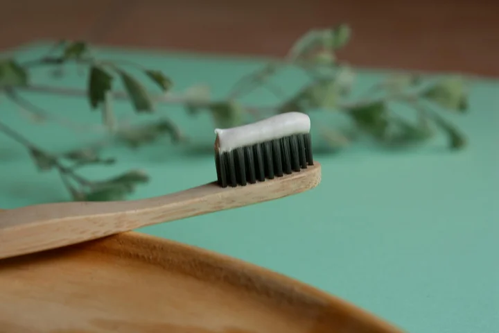 Toothbrush with toothpaste on the bristles resting on a wooden surface, with green leaves in the background