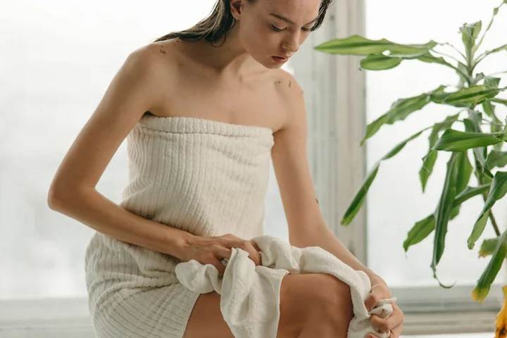 Person wrapped in a white towel sits indoors, examining a towel to address lingering odors.