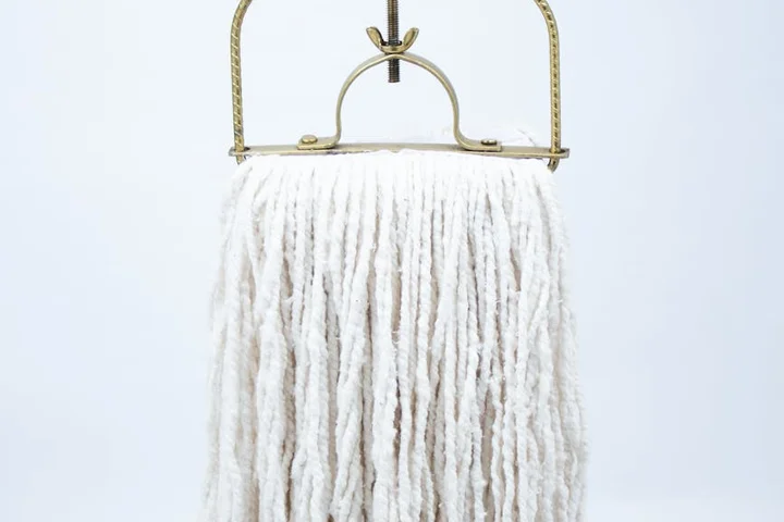 Traditional cotton string mop hanging from a metal wringer against a light background.