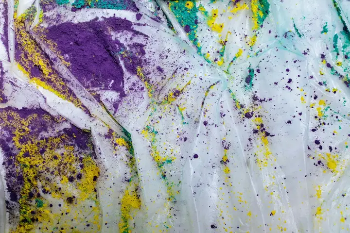 White fabric with vibrant purple, yellow, and green paint splatters and smears, representing tough stains