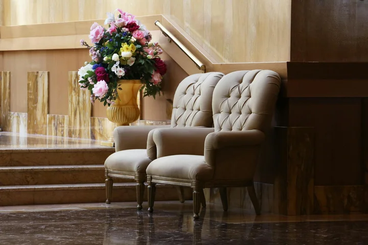 Two beige tufted chairs in a wood-paneled room with a vase of colorful flowers