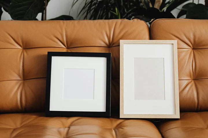 Two framed prints resting on a tan tufted leather couch.