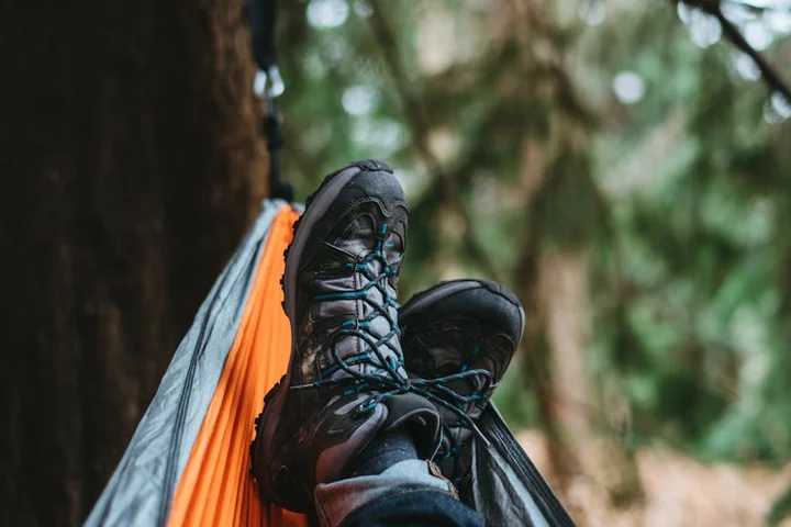 Close-up of black UGG boots with laces resting on orange fabric outdoors, with a blurred forest background.