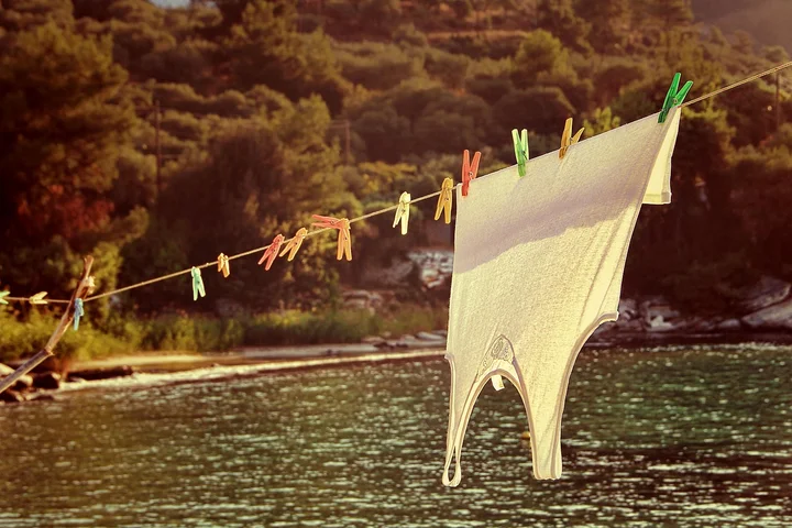 White underwear hanging on a clothesline by a lake with trees in the background.