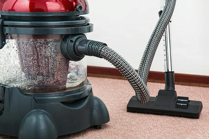 A canister vacuum on a beige carpet with hoses attached, ready to inspect for moisture and padding damage beneath the surface.