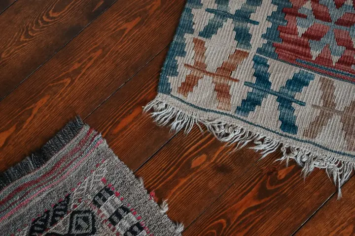 Two vintage woven textiles with geometric patterns and fringed edges laid on a wooden floor.