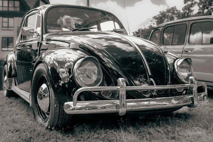 Black vintage Volkswagen Beetle parked on grass with a chrome bumper.