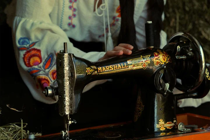 Close-up of a vintage Marshall sewing machine with embroidered fabric, a person's hands guiding the material, illustrating careful handling of delicate textiles.