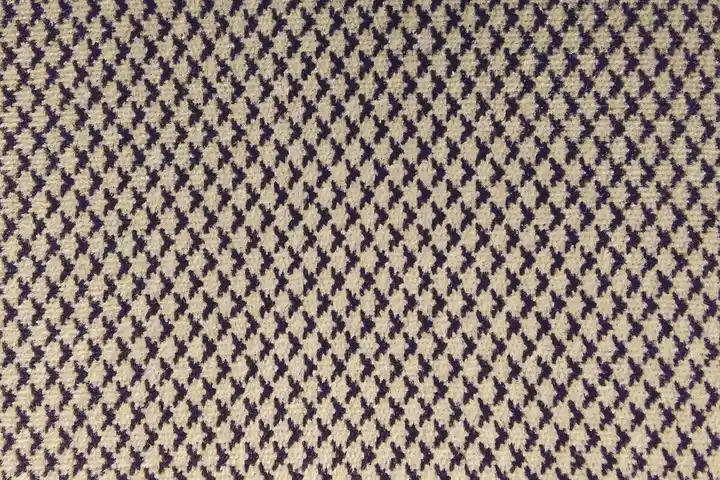 Close-up of a vintage fabric with a repeating purple diamond lattice pattern on a beige background