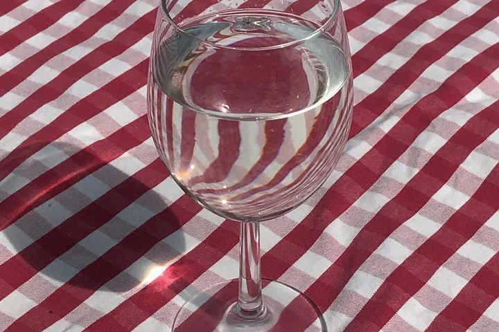 Glass of water on a red-and-white checkered vinyl tablecloth.