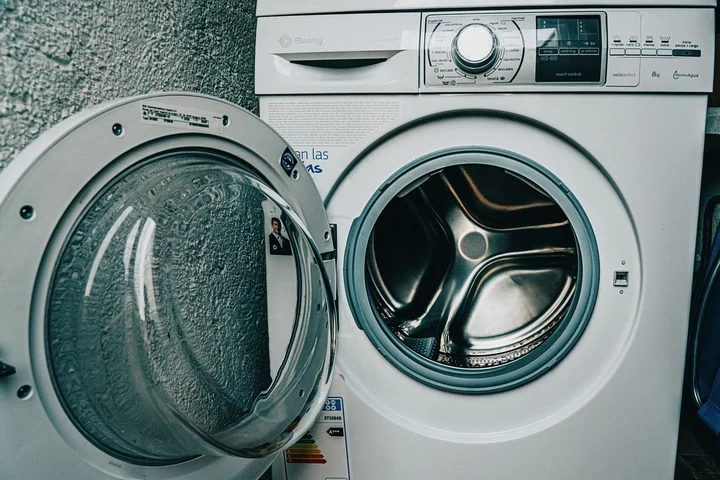 Front-loading washing machine with its door open, exposing the drum in a laundry room.