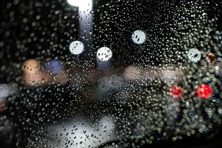Close-up of water droplets on a glass window with blurred city lights in the background.
