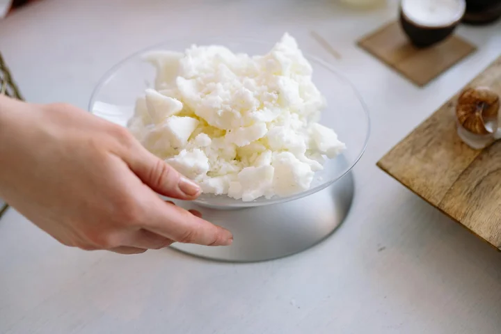 Hands hold a glass bowl filled with white candle wax chunks.