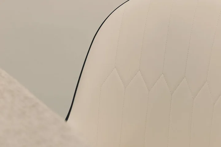 Close-up of white upholstered furniture with diamond stitching and black piping along the edge.