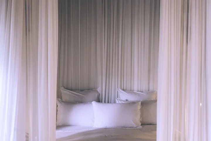 White canopy bed with sheer curtains and white pillows.