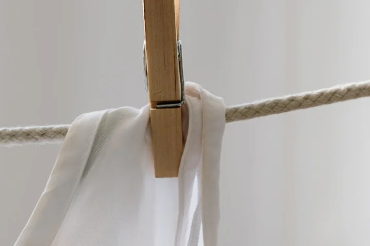 A white shirt draped over a clothesline, secured by a wooden clothespin.