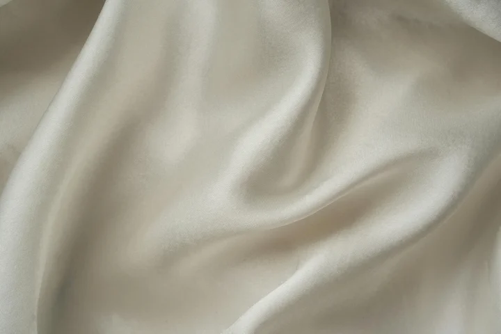 Close-up of smooth white fabric with soft folds and a glossy sheen, likely silk or satin