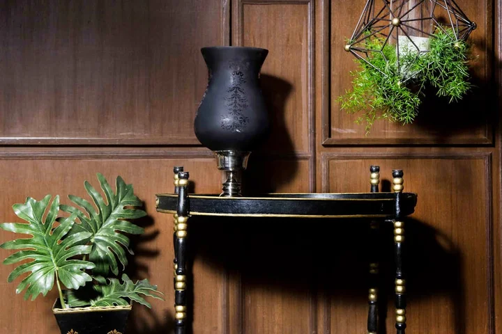 Dark wooden furniture with a small shelf, a black vase, and hanging greenery, illustrating a setting for discussing heat-stain removal on wood.