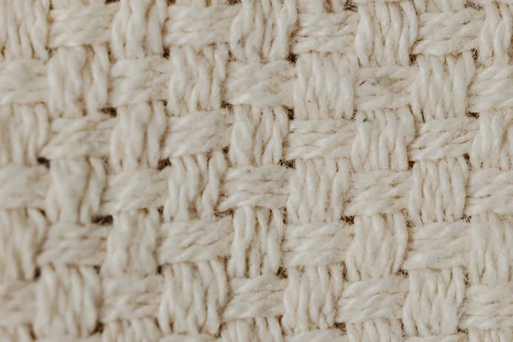 Macro photograph of a light-colored woven fabric showing interlacing fibers.